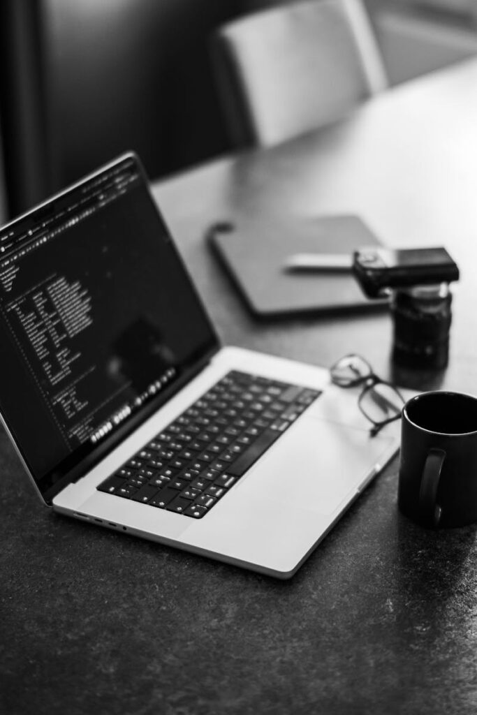 Black-and-white photo of a laptop on a table with coffee, perfect for remote work themes.